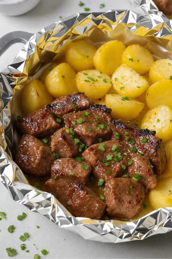 Foil packs opened to reveal juicy steak cubes and golden roasted baby potatoes coated in garlic butter, sprinkled with fresh parsley